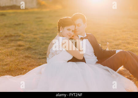 Belle mariée et le marié assis sur une couverture à carreaux avec champagne près de vieux manoir au coucher du soleil Banque D'Images