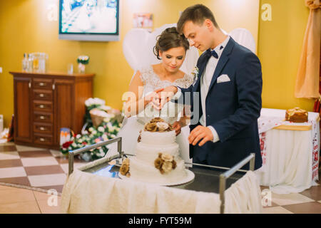 Beau couple marié couper le gâteau de mariage décoré avec des tons beiges et roses de couleur pêche dans le Banque D'Images