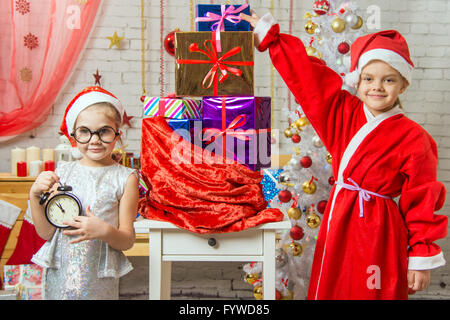 Une jeune fille tenant un réveil, une Fille habillée en père Noël est debout à le sac de cadeaux Banque D'Images