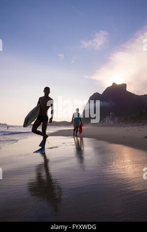 RIO DE JANEIRO - mars 8, 2016 : marche sur São Conrado Bodyboarders plage sous un coucher de soleil silhouette de l'emblématique Pedra da Gávea. Banque D'Images