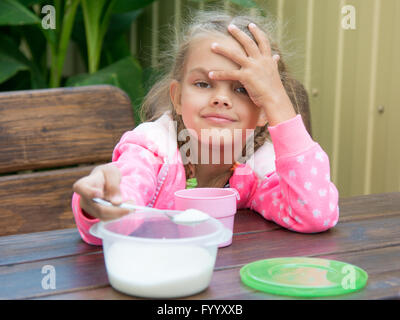 Fille de six ans verse le sucre dans une petite cuillère à café petit déjeuner sur la véranda Banque D'Images