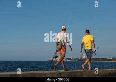 Deux jeunes hommes marchant le long de la partie supérieure de le Malecón (Avenida de Maceo), faisant des cannes à pêche. La Havane (La Habana, Cuba. Banque D'Images