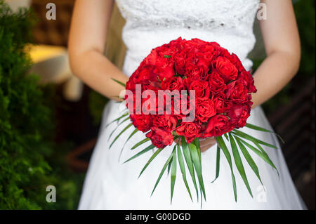 Mariage bouquet de roses rouges et de feuilles dans la main de la mariée Banque D'Images