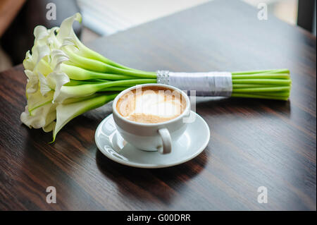 Mariage bouquet de lis calla sur une table avec une tasse de café Banque D'Images