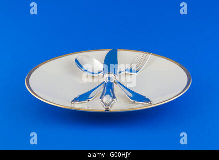 Close up cuillère en argent, fourchette et couteau attaché sur le plat blanc avec un peu de décoration d'or, sur la table bleu Banque D'Images