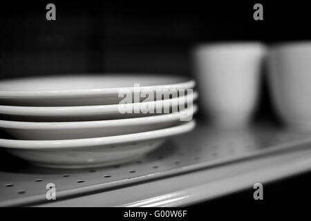 Quatre assiettes en céramique blanche sur plateau avec des tasses blanches en arrière-plan avec une faible profondeur de champ Banque D'Images