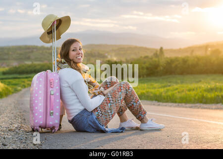 Lonely Girl assis sur la route près de sa valise Banque D'Images