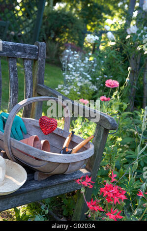 Fauteuil de jardin rustique dans le jardin floral ensoleillé avec des trug accessoires de jardinage et de décoration de l'emblème du coeur Banque D'Images