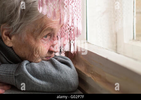 Une femme âgée a tristement par la fenêtre, face close-up. Banque D'Images