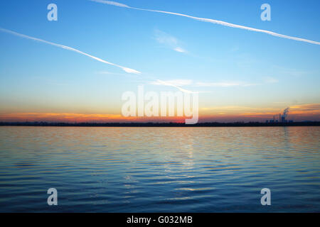 Coucher de soleil sur le lac et une usine à l'horizon Banque D'Images