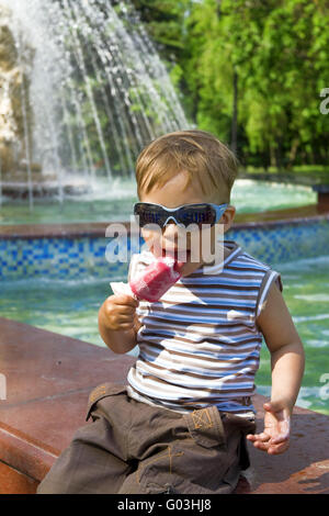 Garçon dans les lunettes de soleil mange la glace contre un founta Banque D'Images