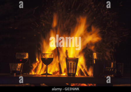 Table avec des verres en face d'un feu de camp la nuit Banque D'Images