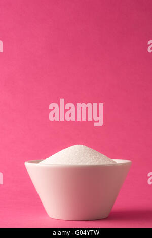 Bol blanc plein de sucre blanc contre fond rose Banque D'Images