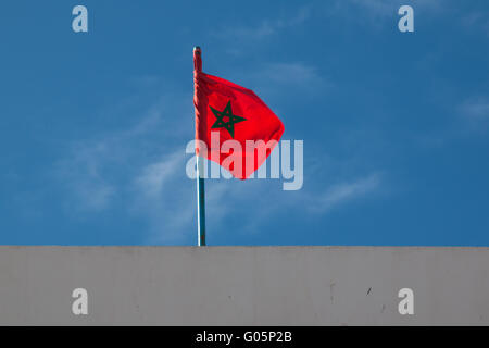 Toit d'un bâtiment. Drapeau marocain dans le vent. Ciel bleu avec quelques nuages dans l'arrière-plan. Banque D'Images