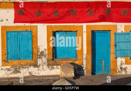 Les volets bleus des fenêtres et portes bleu orange avec les cadres. Vieille maison à Essaouira. Longue bande de drapeau marocain. Banque D'Images