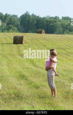 La fille s'assied à mère sur les mains. À l'extérieur. Banque D'Images