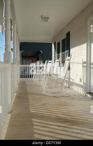 Une rangée de quatre utilisés et patiné en bois laqué blanc de style chaises à bascule sur un porche usés au lever du soleil sur une journée ensoleillée. Banque D'Images