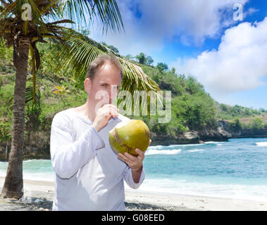 Homme boit le jus de noix de coco à partir d'un écrou sur une plage à Banque D'Images