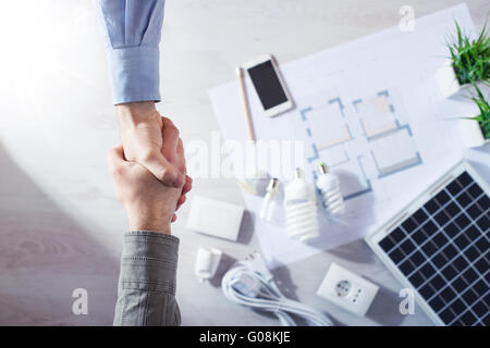 Entrepreneur et client shaking hands close up, l'économie d'énergie lampes CFL, panneau solaire et maison en arrière-plan de projet, haut Banque D'Images