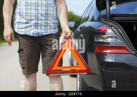 Homme avec triangle de signalisation près de voiture sur la route Banque D'Images