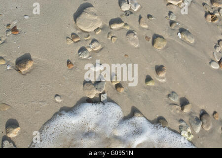 Plage de sable avec des cailloux et des petites vagues floues Banque D'Images