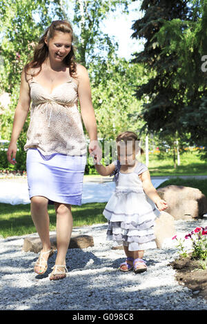 Belle femme enceinte avec son ​​Little fille marcher le long du parc de la ville. Banque D'Images