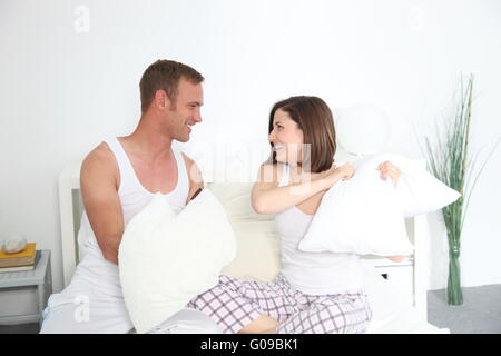 Laughing young couple pillow fighting in bed Banque D'Images
