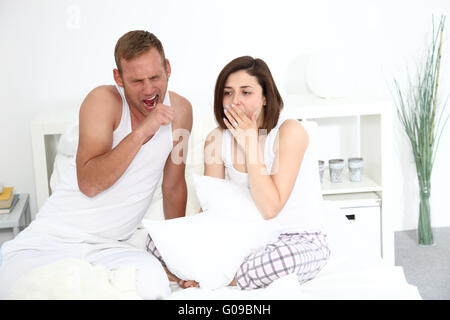 Assez jeune couple yawning in bed Banque D'Images