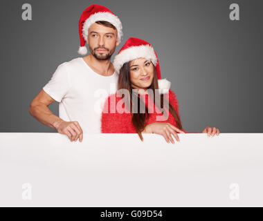 Couple wearing Santa hats holding a blank board Banque D'Images