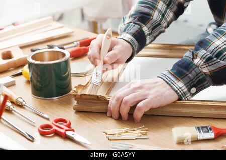 Vernissage de l'homme un cadre en bois mains près des outils de bricolage sur une table de travail Banque D'Images
