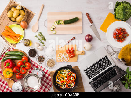 Cuisine végétarienne créative avec ustensiles de cuisine, des légumes frais et de l'ordinateur portable sur une table en bois, vue du dessus Banque D'Images