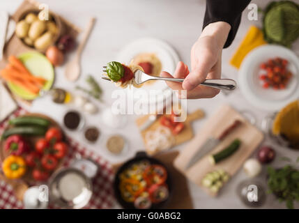 Dans la cuisine du chef tenant une fourchette à spaghetti, sauce tomate et basilic, les ingrédients alimentaires et les ustensiles sur arrière-plan, Vue de dessus Banque D'Images