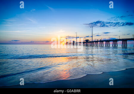 Le soleil levant se profile à travers les nuages et se reflète dans les vagues par le Nags Head fishing pier sur les Outer Banks de Caroline du Nord. Banque D'Images