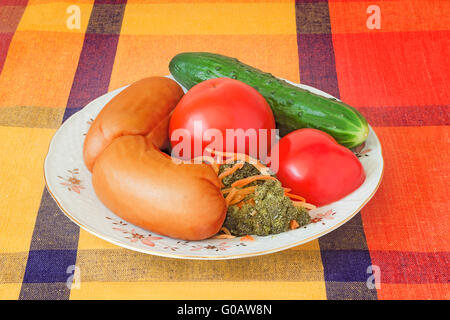 Deux grosses saucisses et légumes sur une assiette blanche. Banque D'Images