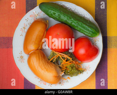 Deux grosses saucisses et légumes sur une assiette blanche. Banque D'Images