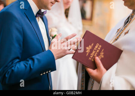 Le prêtre l'anneau sur le doigt de robes de marié au cours de mariage à l'église Banque D'Images