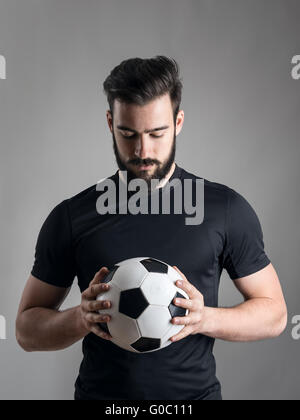 Portrait du joueur de football intense holding et à la balle à l'arrière-plan gris axé au studio. Concept de détermination. Banque D'Images