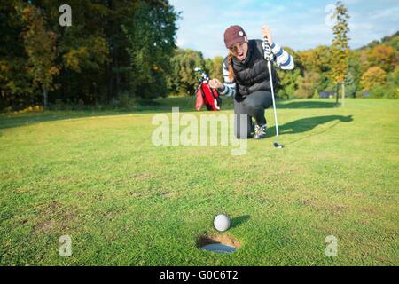 Femme - joueur de golf sur les genoux et les bras levés avec putter dans la main en gagnant posent sur golf green d'être heureux comme balles de golf Banque D'Images