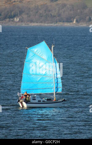 L'yacht Caber, avec un voile bleu de couleur vive, en passant Cloch Point sur le Firth of Clyde. Banque D'Images