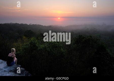 Un solo female hiker regarder le lever du soleil sur la jungle tropicale de l'ancien temple maya numéro 4 sur le site archéologique de Tikal un ancien centre urbain de la civilisation maya précolombienne situé dans la région archéologique du bassin au nord du Petén au Guatemala Banque D'Images