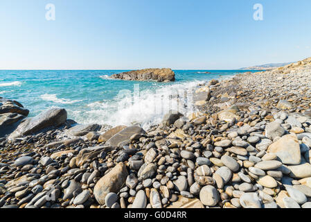 Les graviers de vagues se brisant sur l'eau, les cailloux et les rochers d'une plage vide dans la rude côte rocheuse de la Ligurie, au nord de l'Italie. Cl Banque D'Images