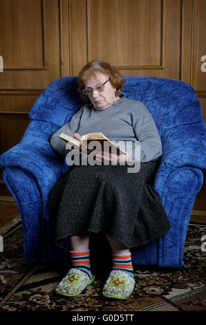 La vieille femme est assise dans un fauteuil et lit le livre Banque D'Images