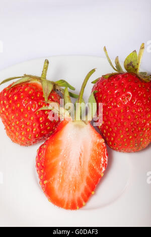 La moitié des fraises mûres et juteuses sur une plaque avec deux fruits entiers. close-up. Banque D'Images