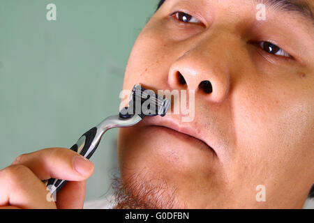 Young Asian man shaving ses cheveux du visage sans crème Banque D'Images