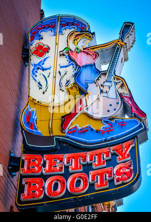 Enseigne au néon publicitaire coloré de femme avec guitare assis sur de grosses bottes de cowboy boot pour Betty Co., à Music City, Nashville, TN Banque D'Images