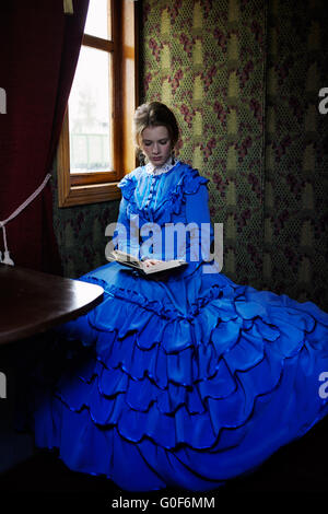 Jeune femme en bleu vintage dress la lecture du livre en train de retro coupé Banque D'Images