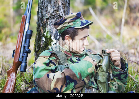 Jeune recrue avec fusil optique en forêt près de tr Banque D'Images