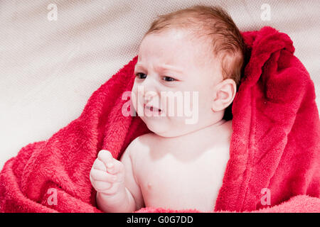 Lovely baby 3 mois en position allongée sur un lit recouvert d'une couverture rouge. Banque D'Images