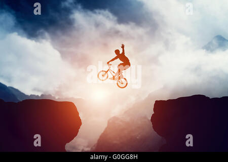 Man sur vélo BMX au précipice dans la montagne au coucher du soleil. Raising hand montrant bonjour geste. Sport extrême Banque D'Images