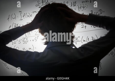 Student holding sa tête à la recherche de formules mathématiques complexes sur tableau blanc. Problème à résoudre Banque D'Images